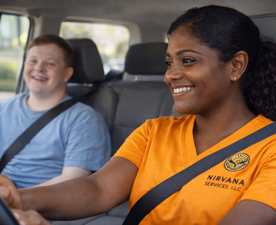 A direct support professional driving a young man to an appointment, both wearing seat belts.
